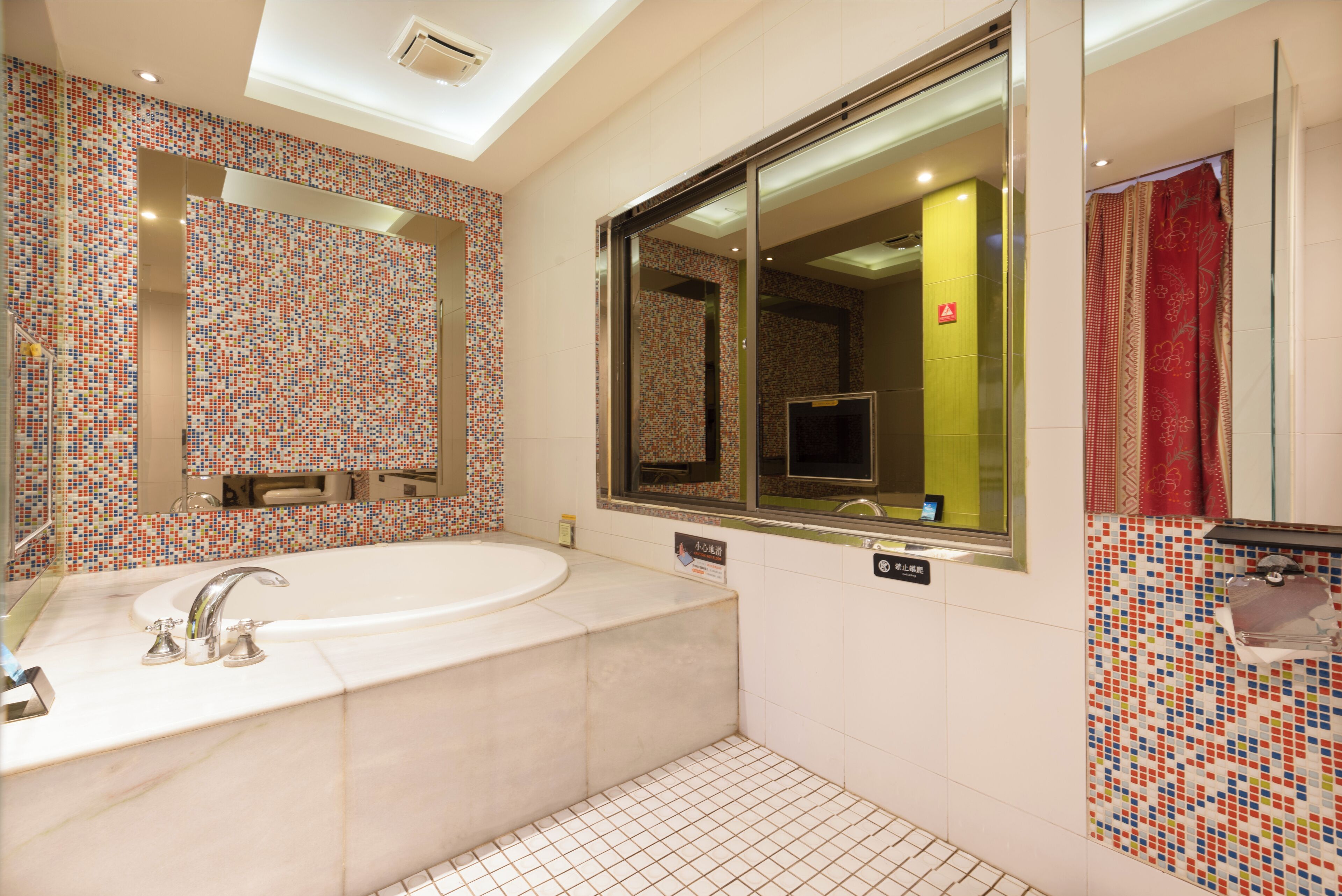 A modern bathroom with a large bathtub, a mirror, and a tiled wall.