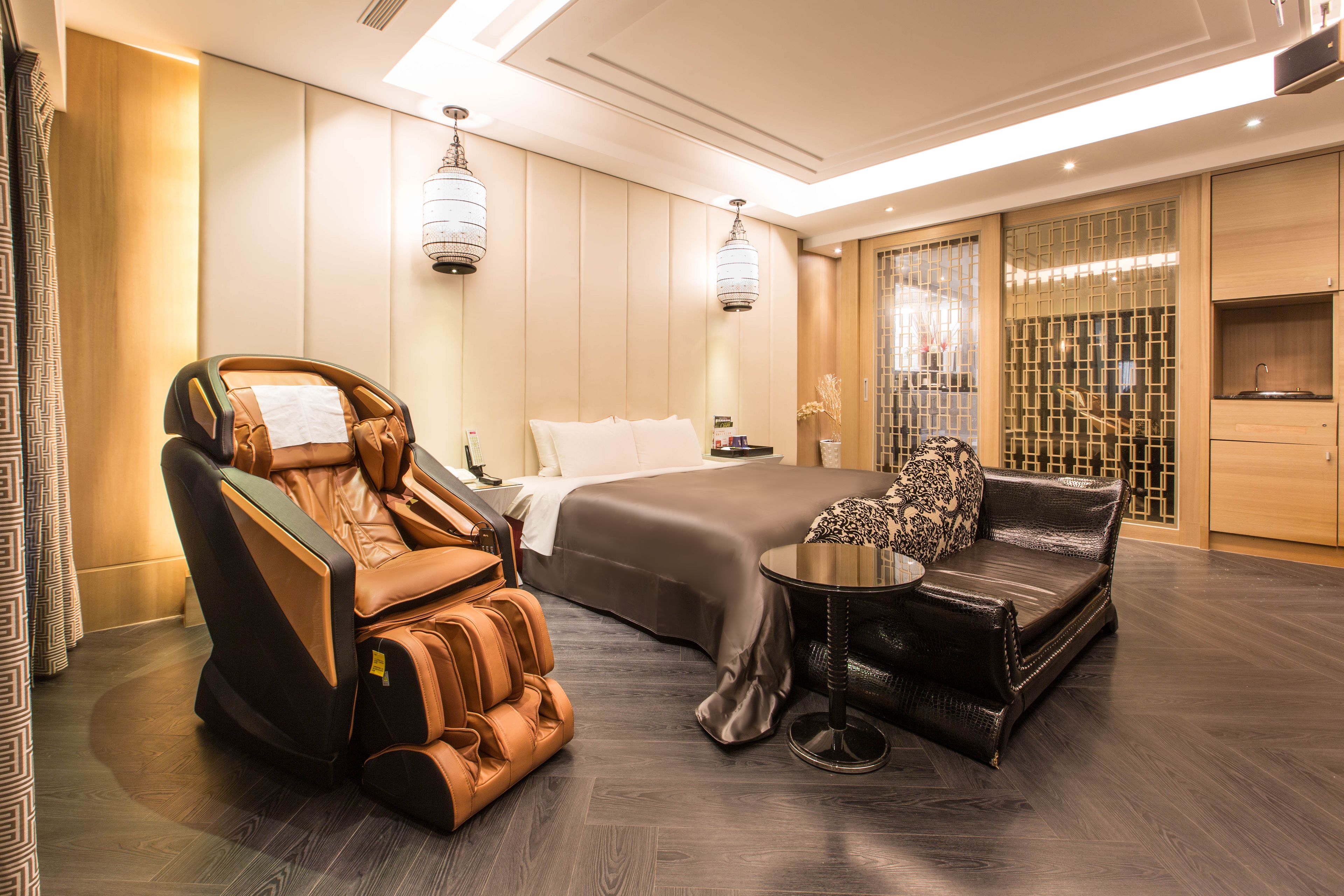 Una habitación de hotel moderna con una silla de masaje, un sofá, una cama y una mesita.