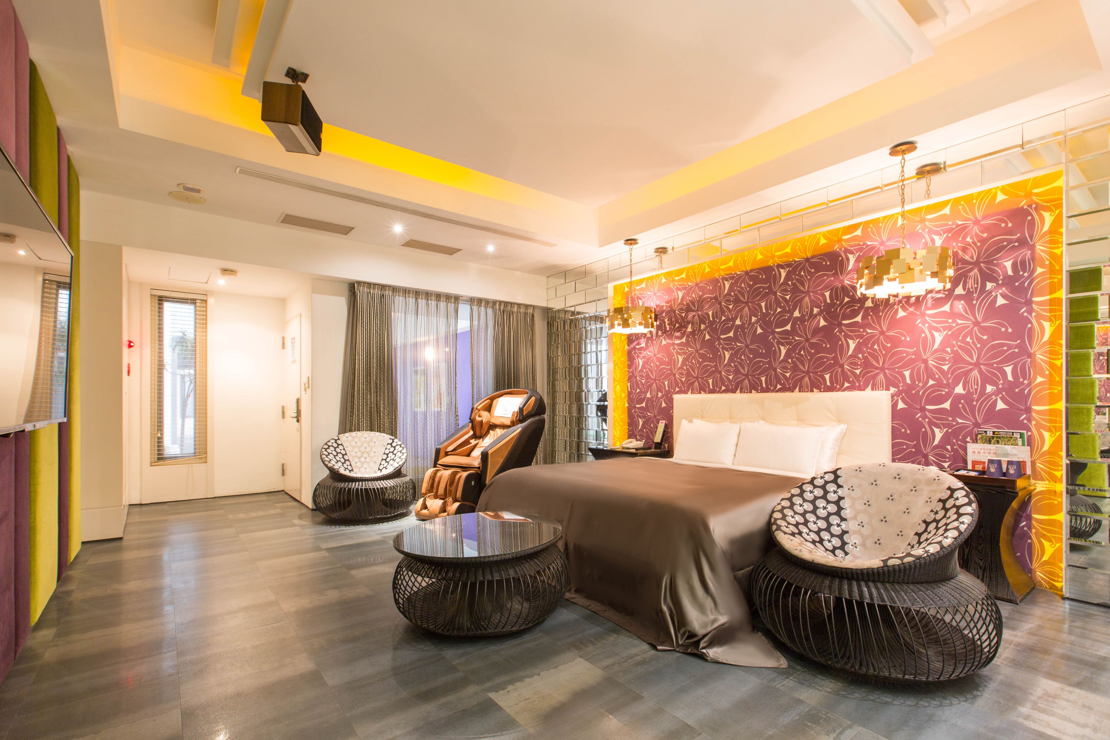 A modern hotel room with a large bed, two round side tables, a massage chair, and a decorative wall.
