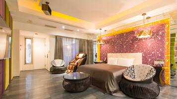 A modern hotel room with a large bed, two round side tables, a massage chair, and a decorative wall.