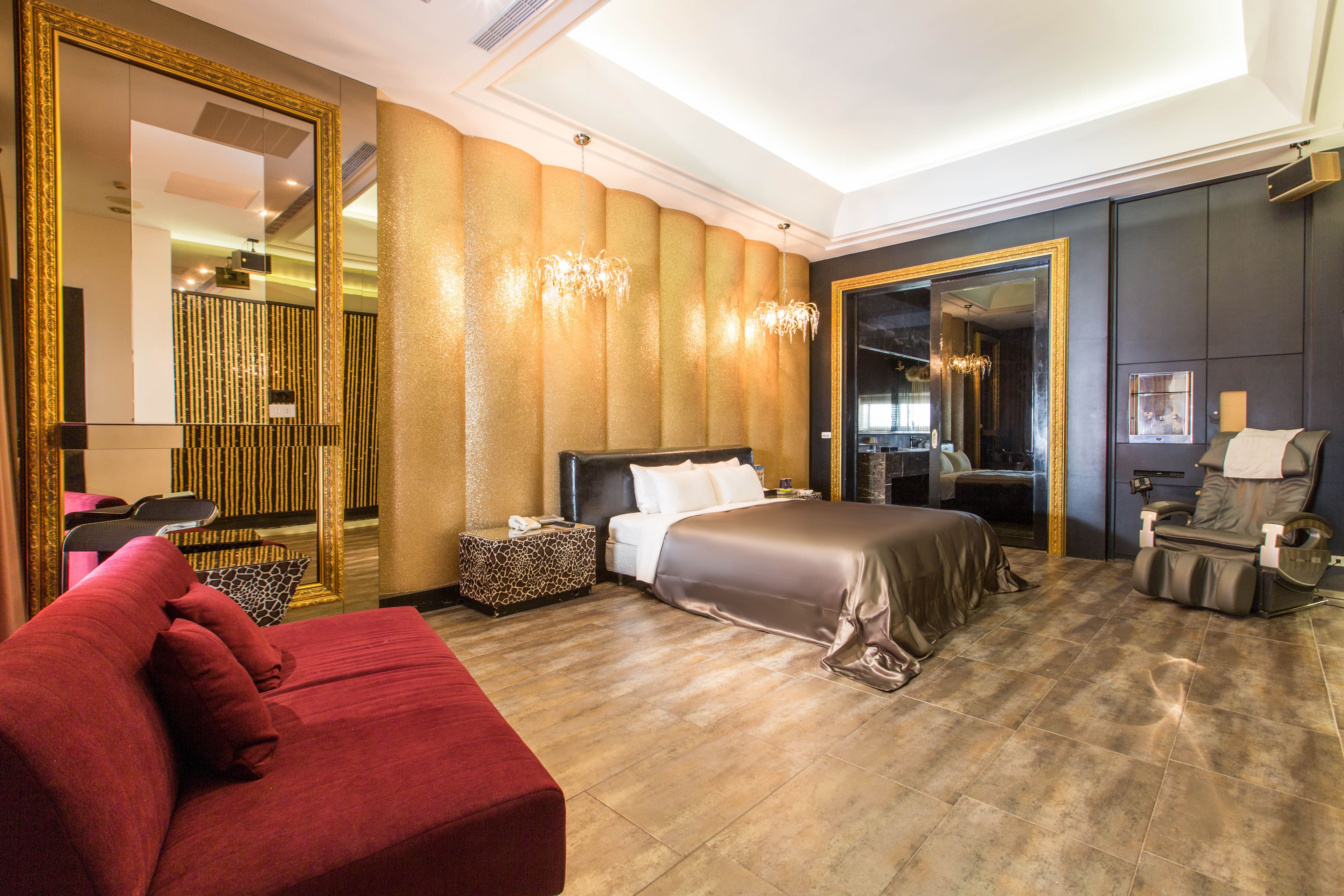 A spacious hotel room with a large bed, a red sofa, a mirror, and a massage chair.