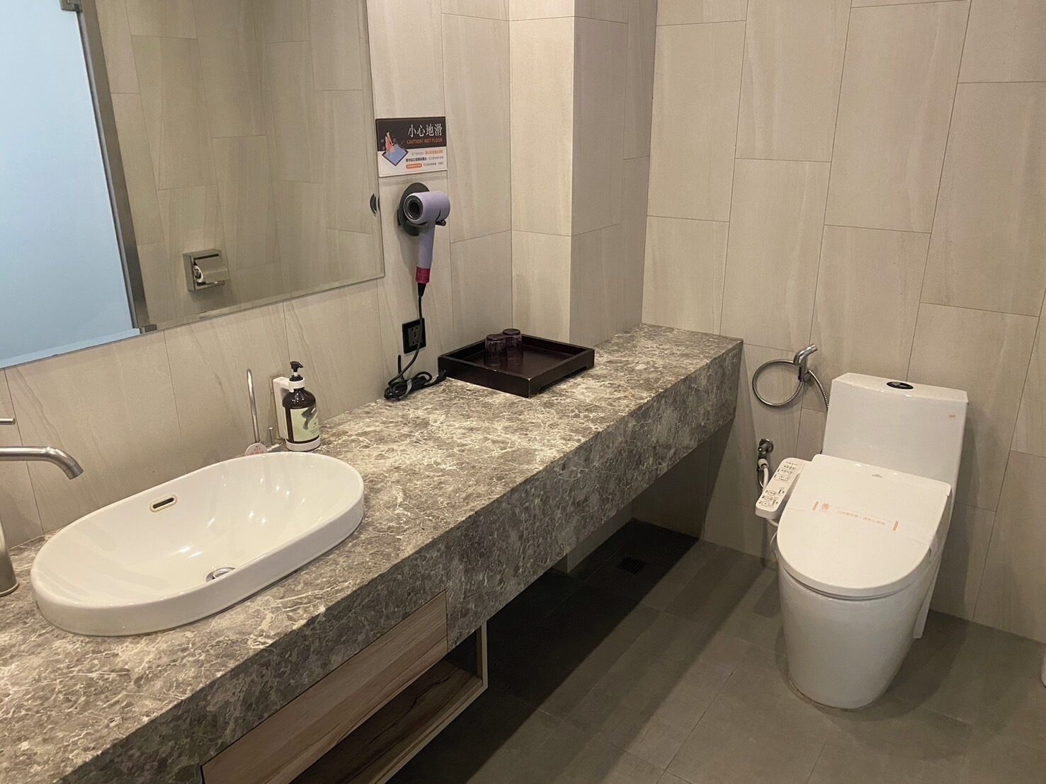 Een moderne badkamer met een marmeren wastafel, een spiegel, een haardroger en een toilet.