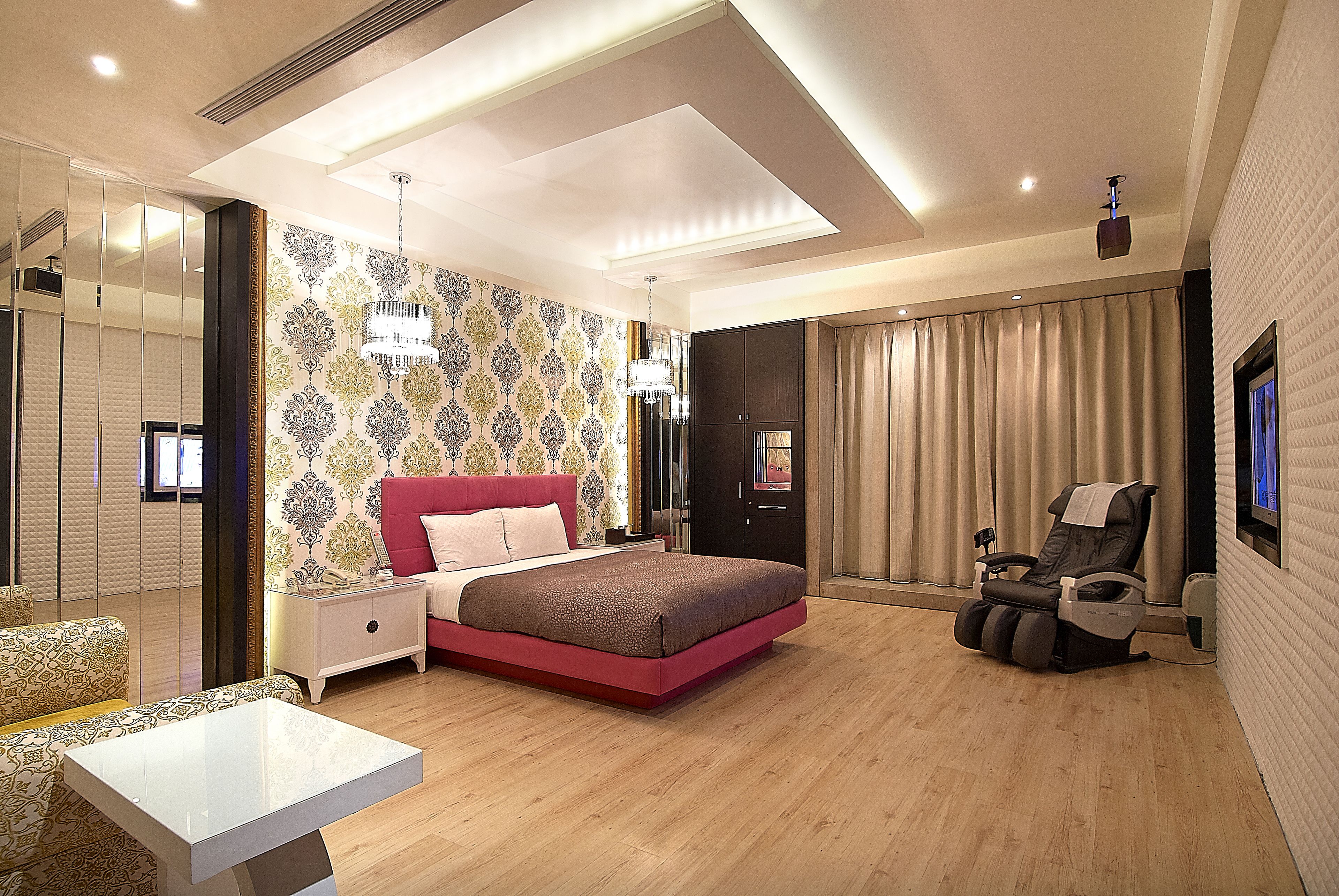 Un dormitorio moderno con una cama grande, una silla de masaje, una mesita de noche y un espejo.