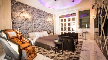 A modern bedroom with a massage chair, a large bed, a sofa, and a vanity with a mirror.