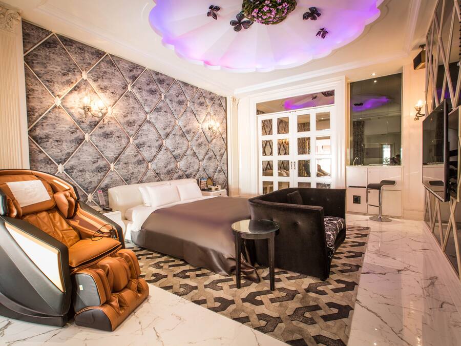 Un dormitorio moderno con sillón de masaje, cama grande, sofá y tocador con espejo.