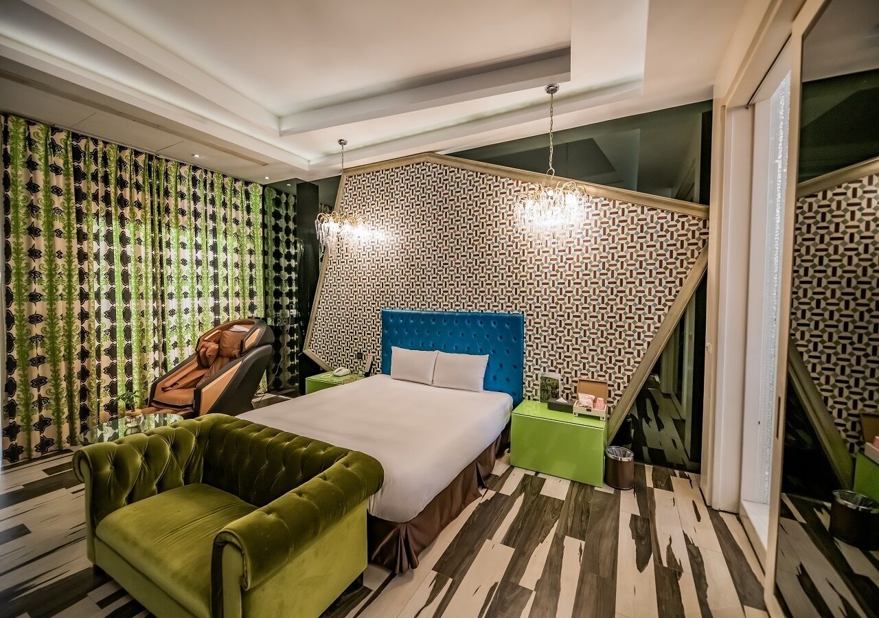 A modern hotel room with a large bed, green armchair, and a massage chair.