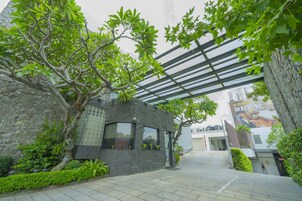 Un edificio de piedra con diseño moderno, un paseo techado y abundante vegetación.