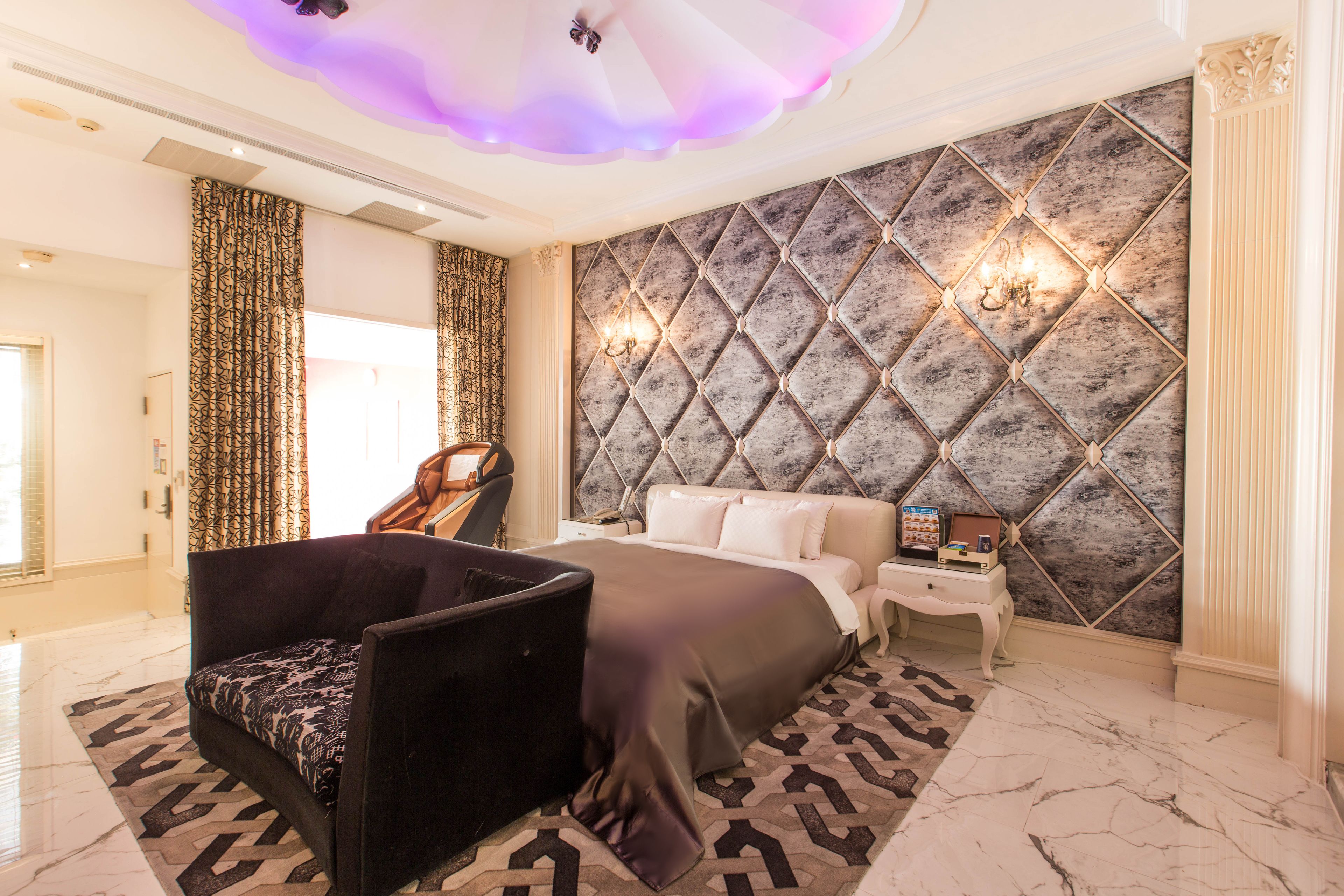 A modern bedroom with a large bed, a seating area, and a decorative wall.
