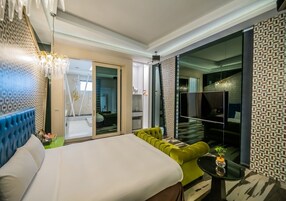 Una habitación de hotel moderna con una cama grande, un sofá verde, una mesita pequeña y un espejo grande.