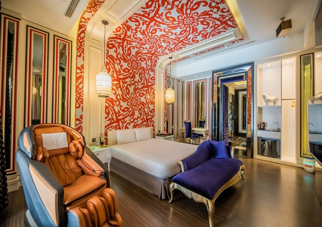 A spacious hotel room with a large bed, a massage chair, and a vanity with a mirror.