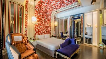 A spacious hotel room with a large bed, a massage chair, and a vanity with a mirror.