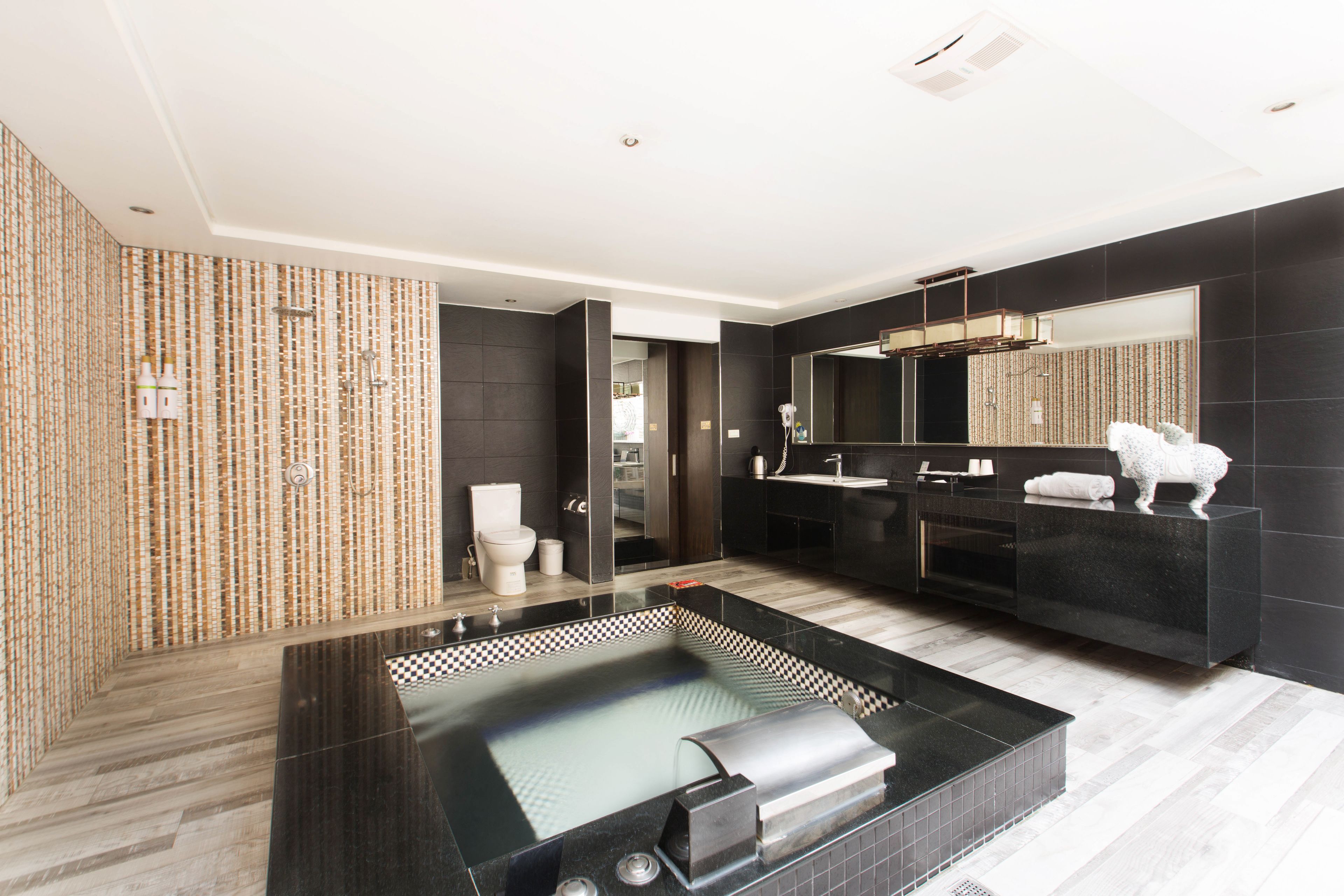 A modern bathroom with a large black bathtub, a separate shower area, and a vanity with a mirror.