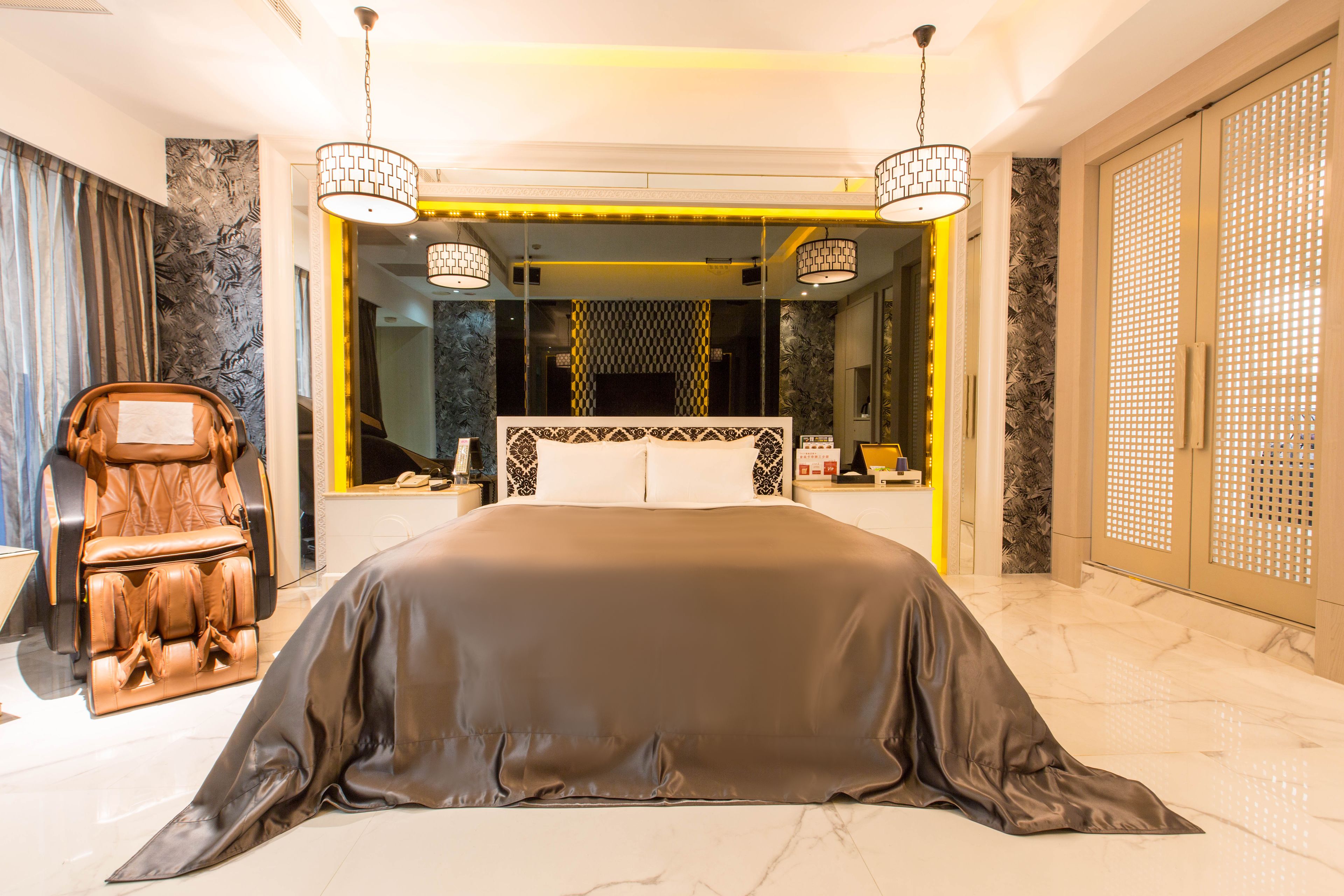 A modern bedroom with a large bed, a massage chair, and a mirror reflecting the room.