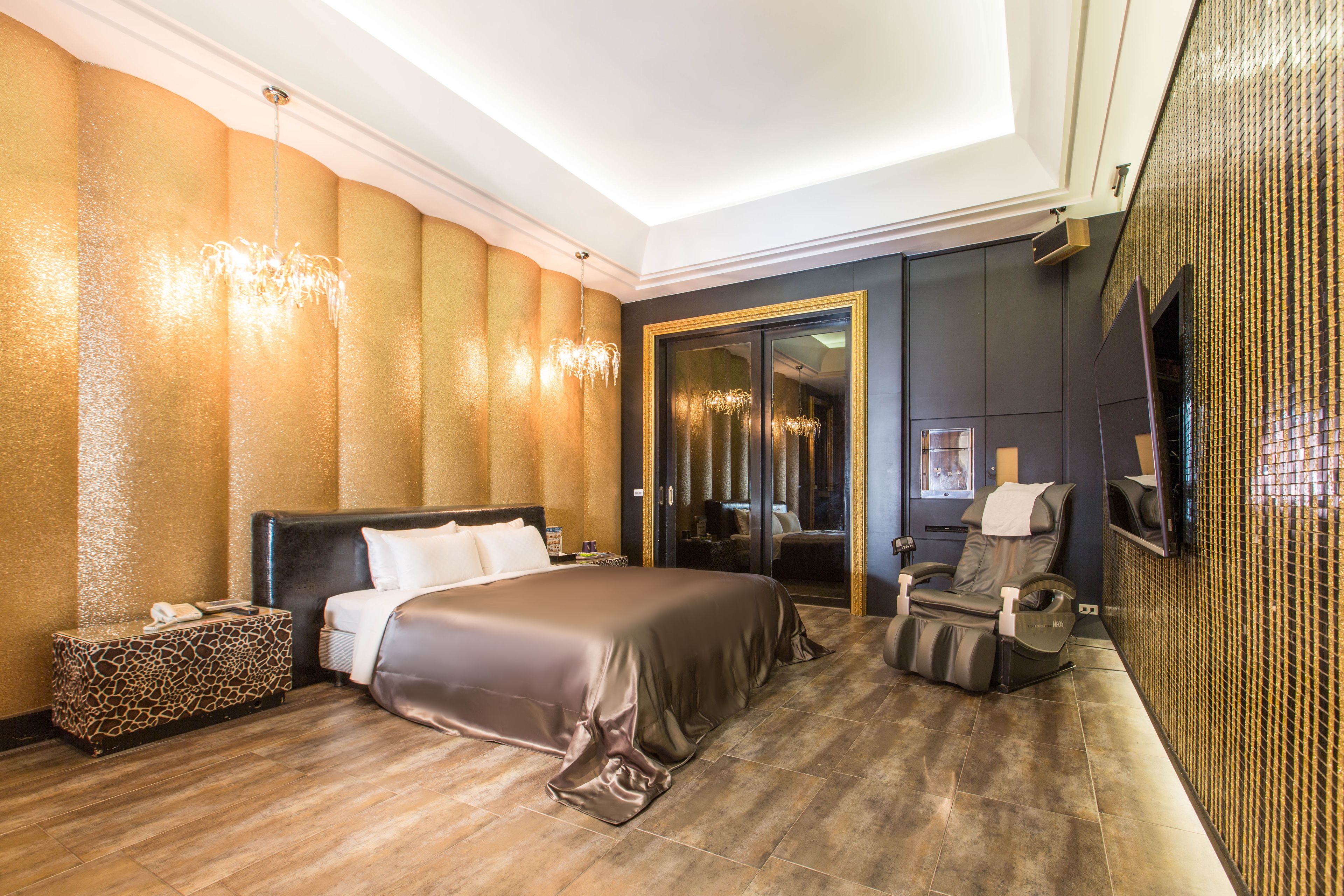 Une chambre d’hôtel dotée d’un grand lit, d’un fauteuil massant, d’un minibar et d’un miroir avec un cadre doré.