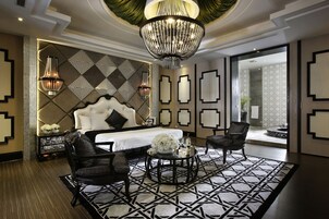 Una habitación de hotel moderna con una cama grande, dos sillones, una mesa de centro redonda y un candelabro.