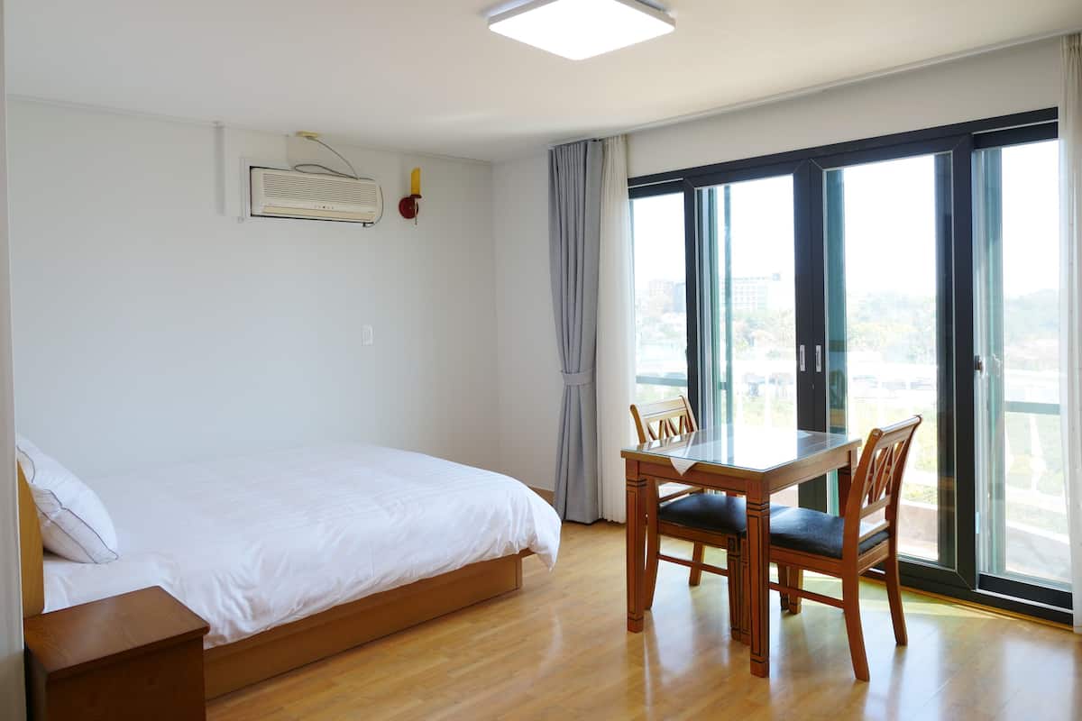 Quarto com cama, escrivaninha com cadeiras, janela com cortinas e luminária no teto.