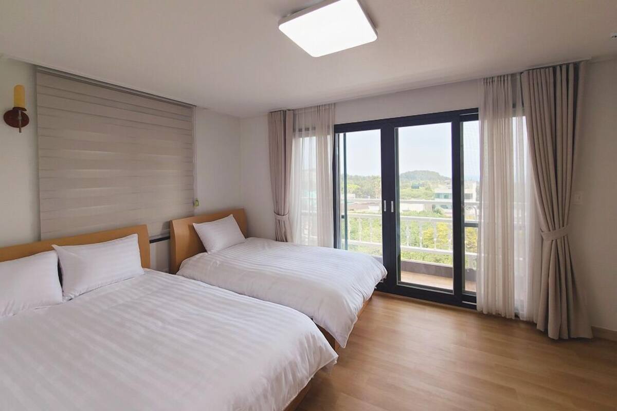 Quarto de hotel com duas camas, uma grande porta de correr de vidro para uma varanda e uma luminária no teto.