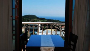 A balcony with a table and chairs, overlooking a scenic view of a coastline and hills. - Hera's Castle (Seogwipo)