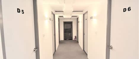 Een hal met deuren met de aanduiding D5 en D6, een brandblusser en een ventilatieopening in het plafond.