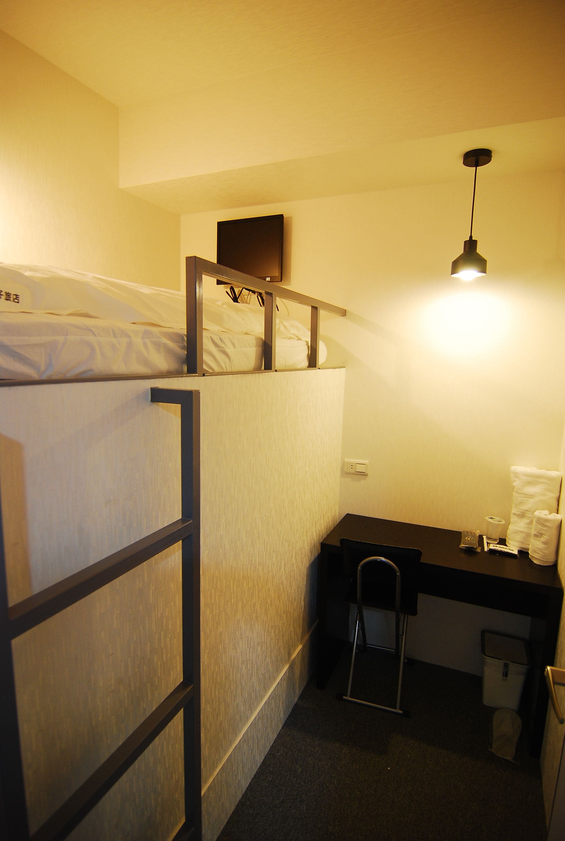 A compact hotel room with bunk beds, a desk, a chair, and a small workspace.