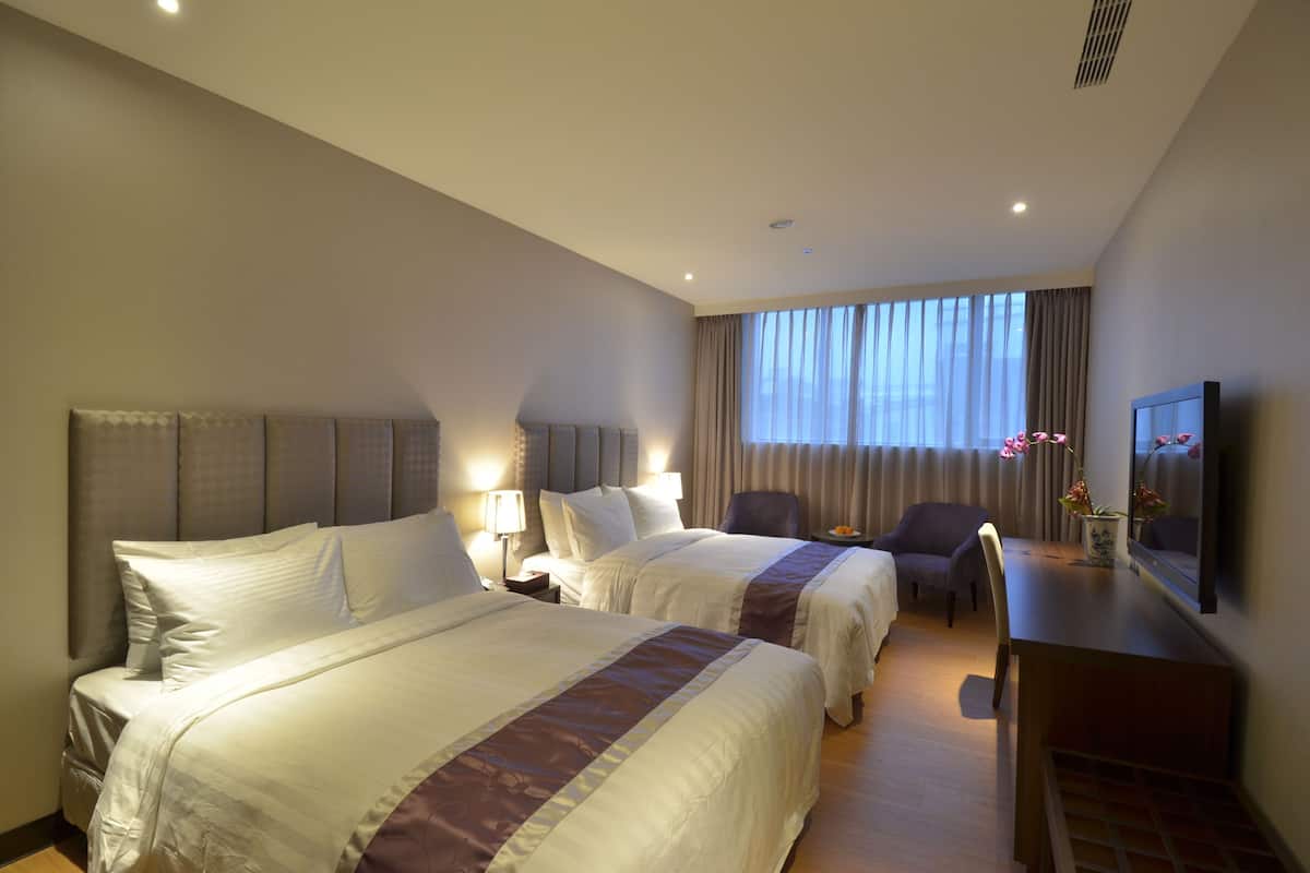 A hotel room with two beds, a desk, a chair, a TV, and a window with curtains.