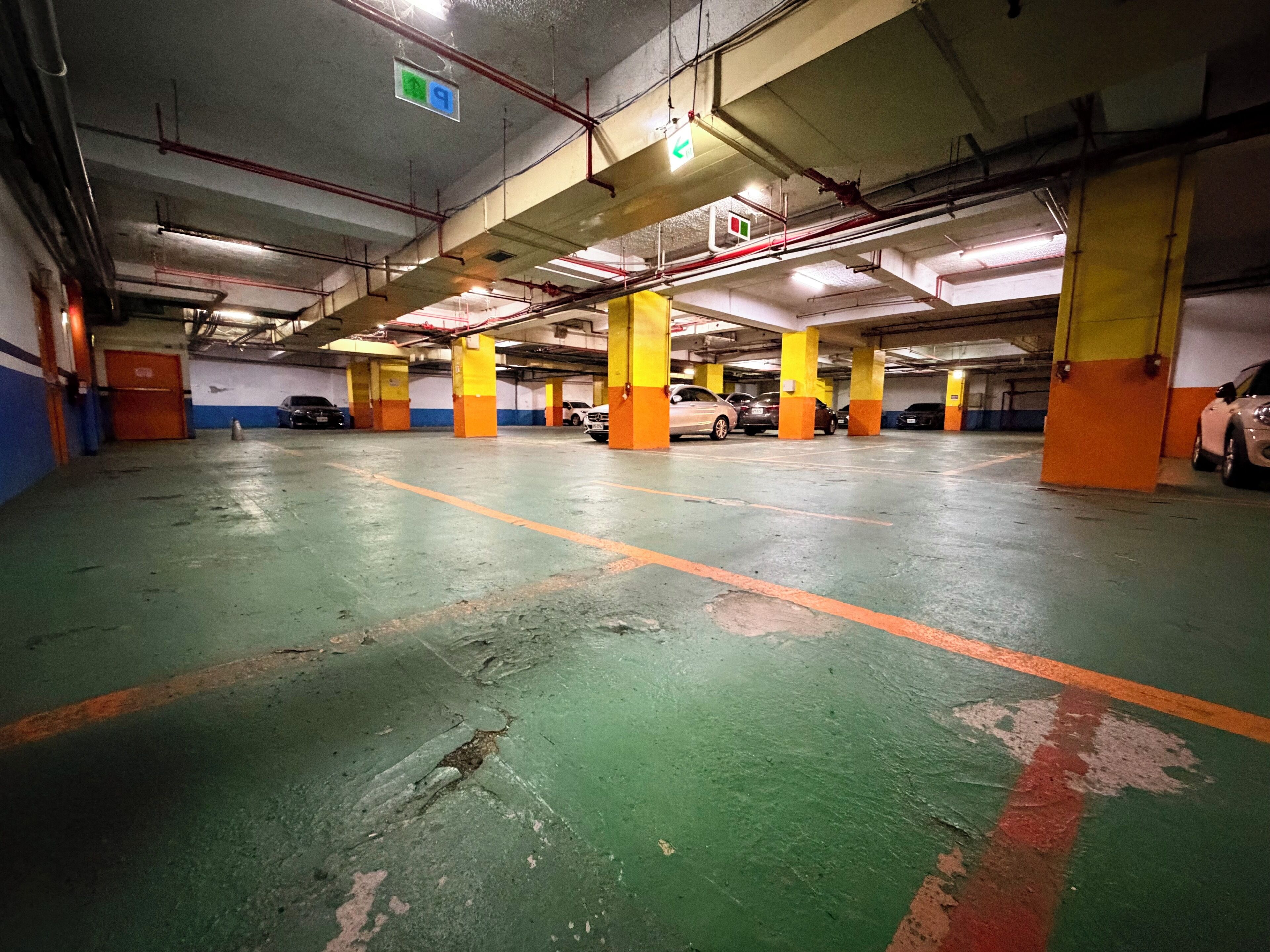 Un estacionamiento de varios niveles con pisos pintados de verde y naranja, pilares de concreto e iluminaci ón colgante.