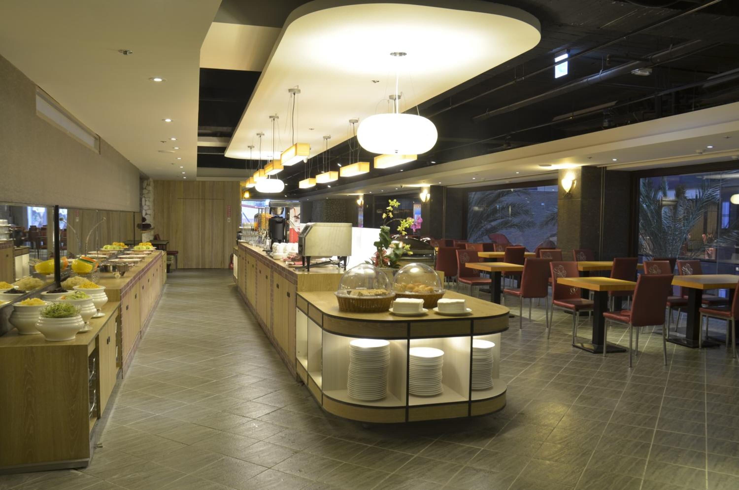 A modern hotel dining area with a buffet setup, a central island with seating, and a view of the outdoors.
