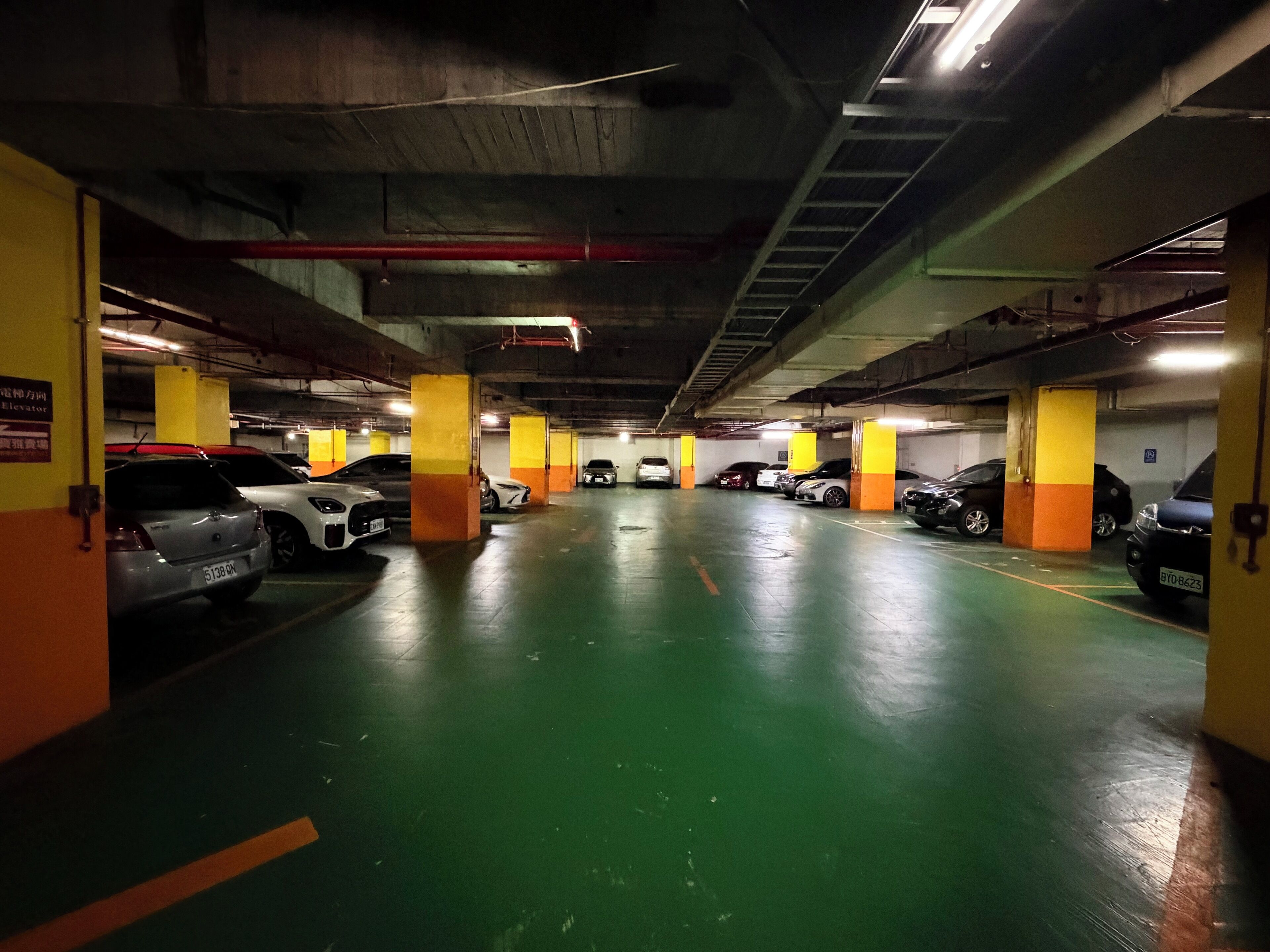 A multi-level underground parking garage with cars parked in rows, concrete pillars, and overhead lighting.