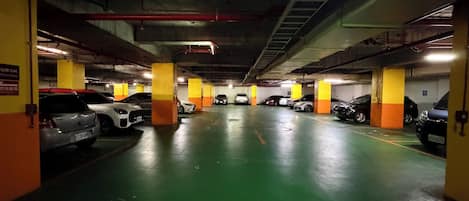 A multi-level underground parking garage with cars parked in rows, concrete pillars, and overhead lighting.