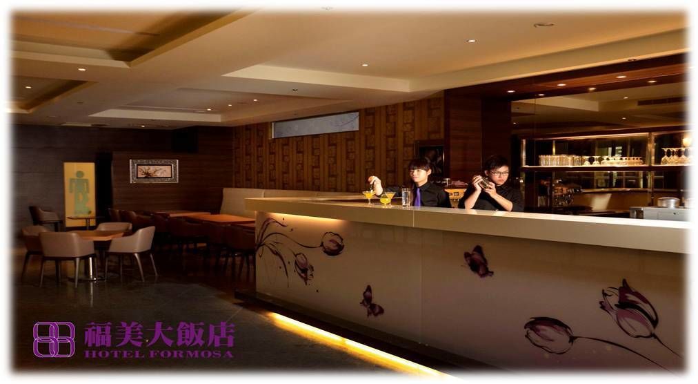 A hotel reception area with a counter, seating area, and a wall with floral designs.