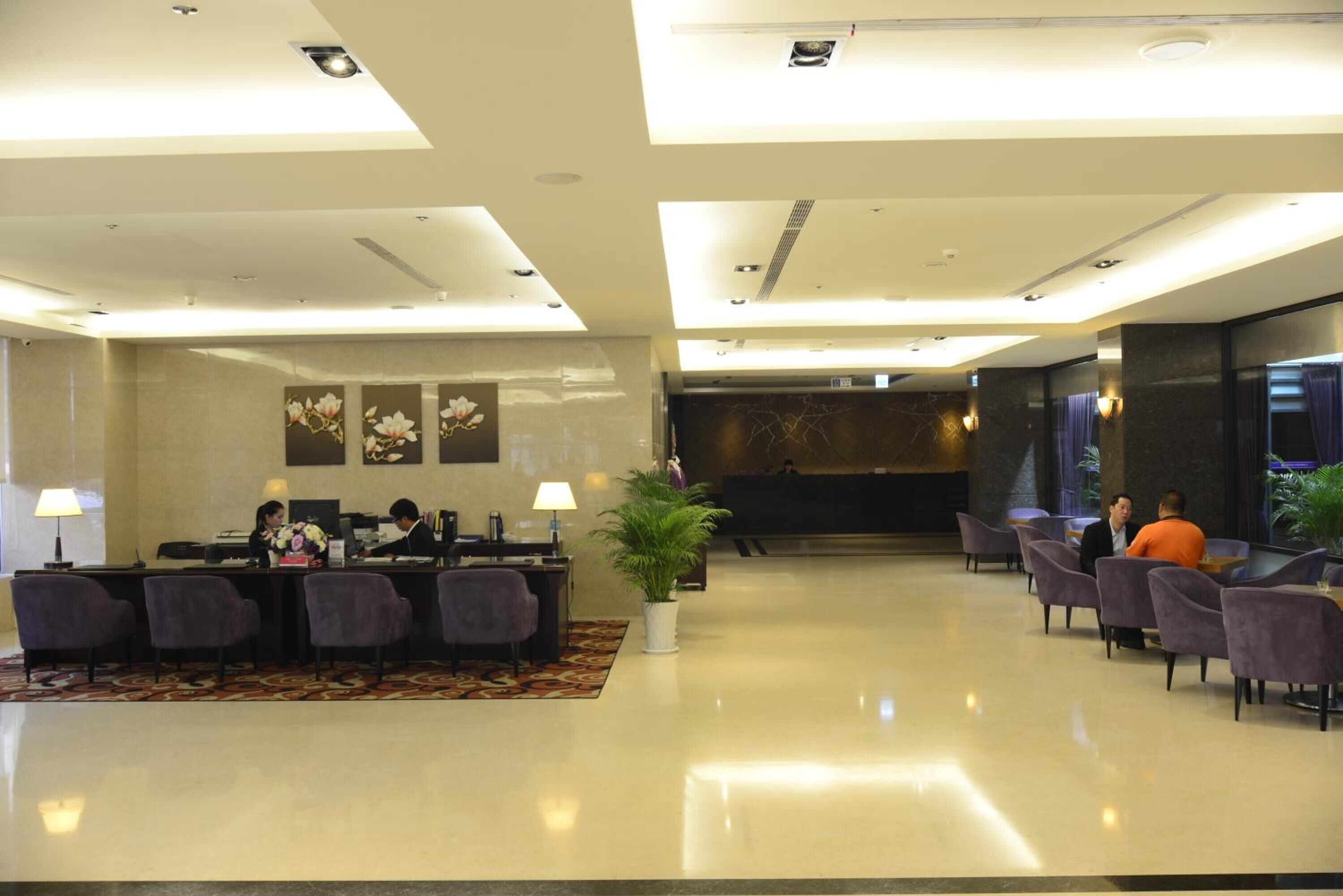 Vestíbulo de hotel con mostrador de recepción, zona de estar y una planta grande.