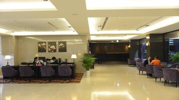 Vestíbulo de hotel con mostrador de recepción, zona de estar y una planta grande.