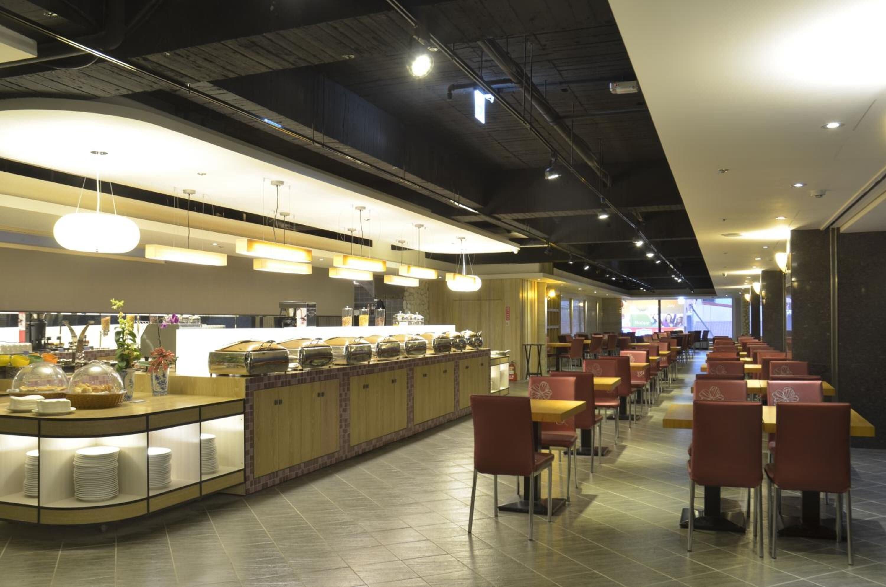 A modern restaurant with a buffet counter, multiple dining tables, and chairs.