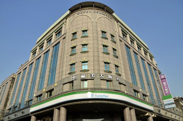 Un hotel con fachada curva, múltiples ventanas y un letrero verde y blanco de FamilyMart a nivel de calle.