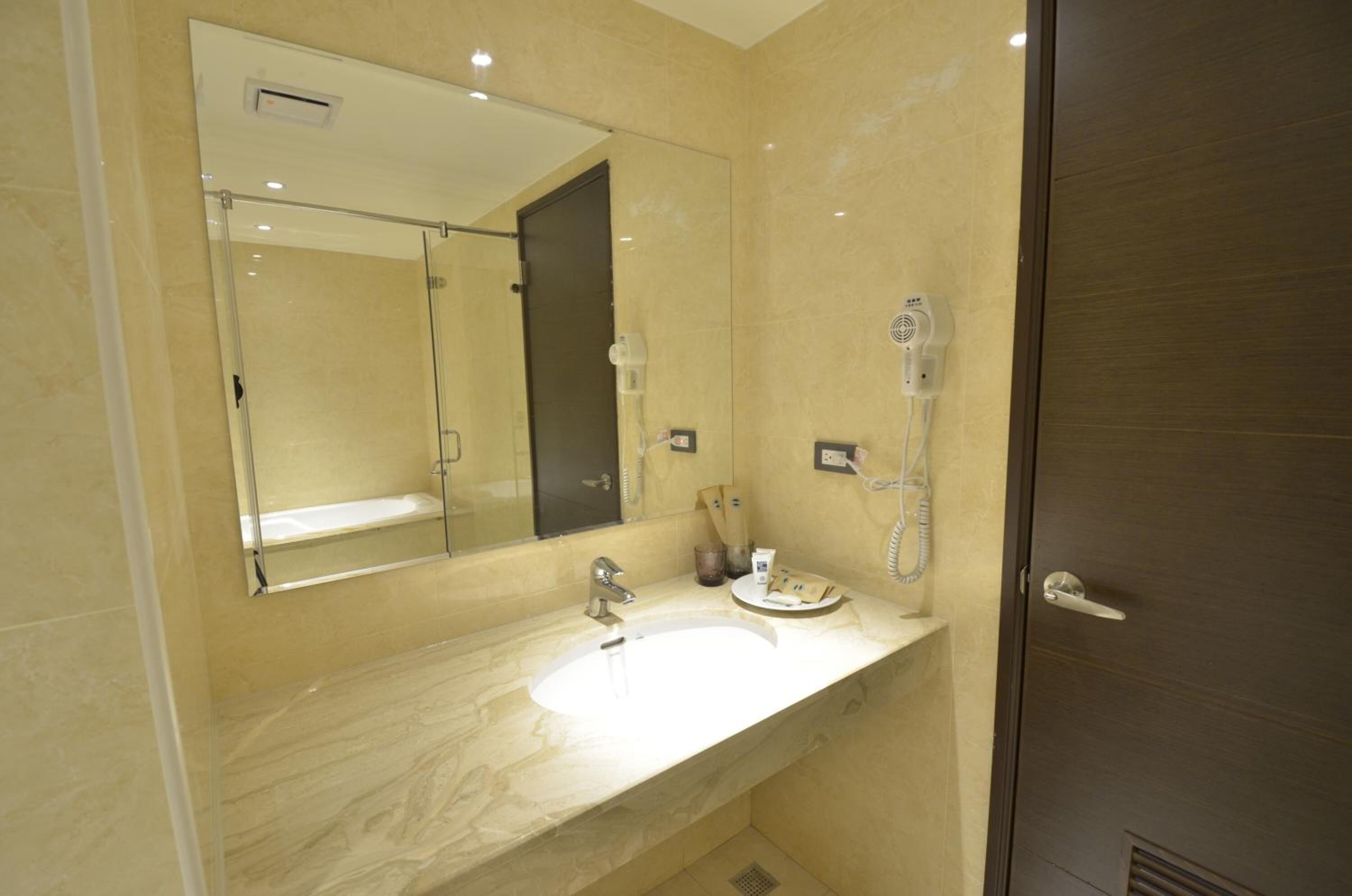 A modern bathroom with a large mirror, a sink, a handheld showerhead, and a towel rack.