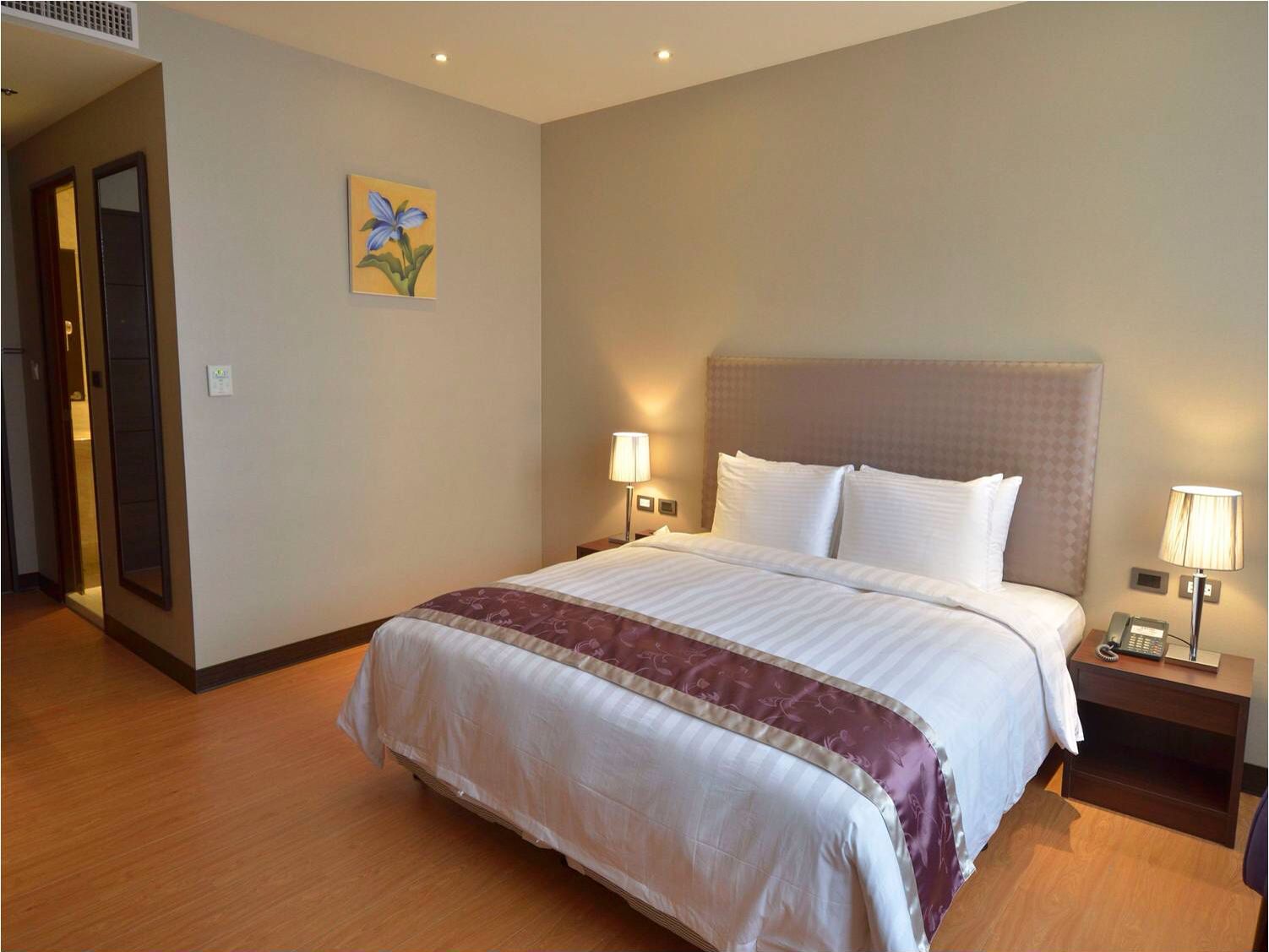 A hotel room with a large bed, two bedside lamps, a nightstand with a phone, and a painting on the wall.