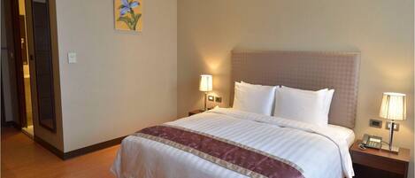 A hotel room with a large bed, two bedside lamps, a nightstand with a phone, and a painting on the wall.