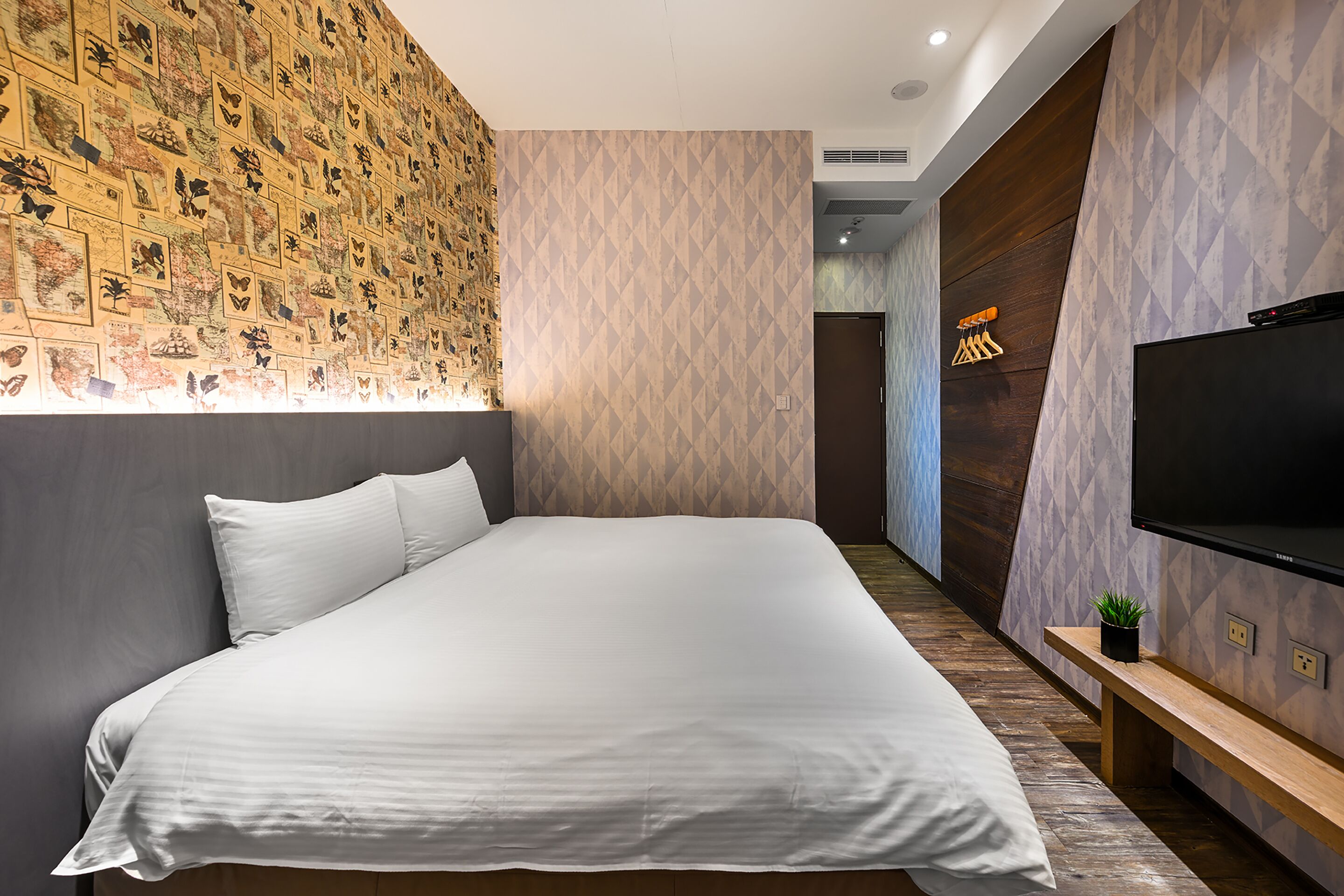 A modern hotel room with a large bed, a TV, and a wall decorated with butterfly illustrations.