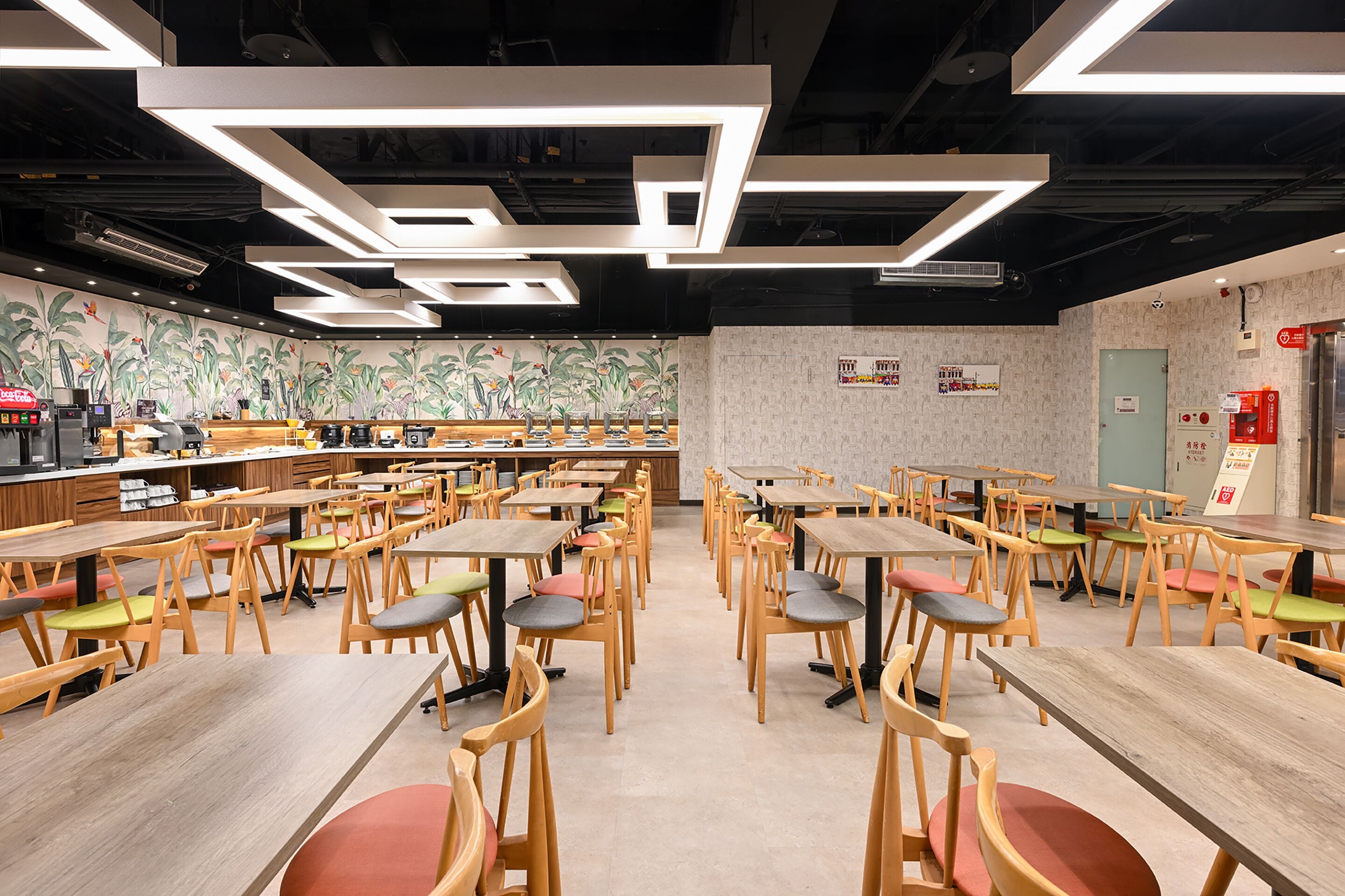 A spacious dining area with multiple wooden tables and chairs, modern ceiling lighting, and a mural on the wall.