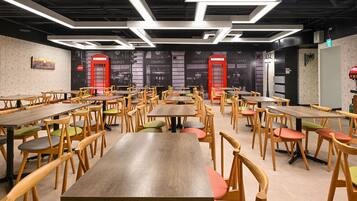 A spacious dining area with multiple wooden tables and chairs, featuring a modern ceiling design and red doorways.