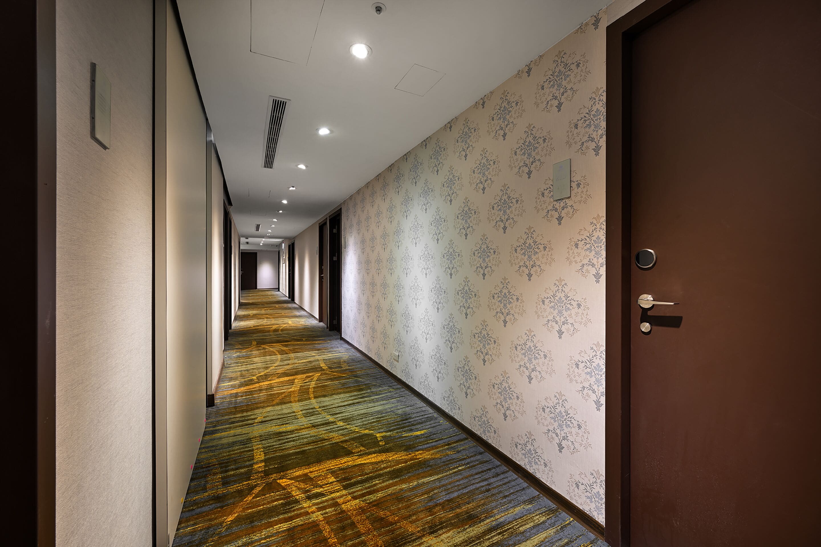 A hotel hallway with patterned wallpaper and a carpeted floor.
