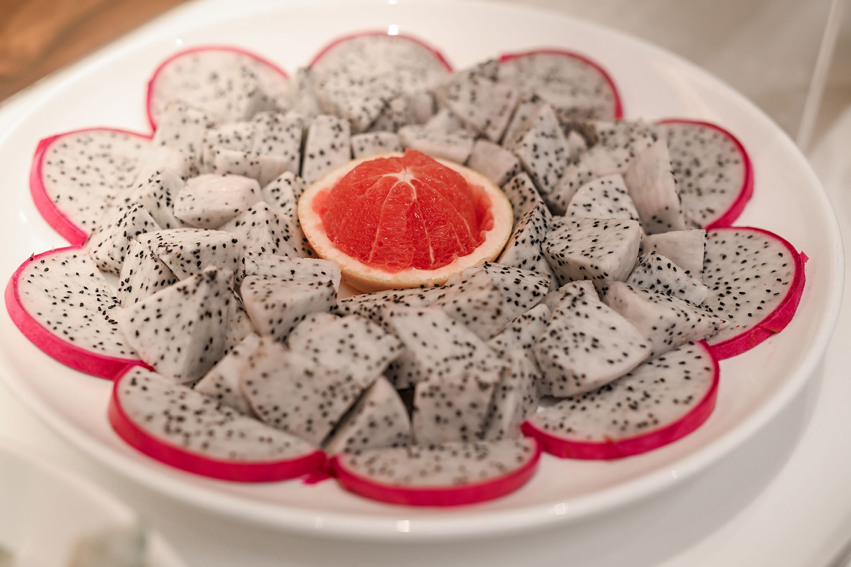 Une assiette blanche avec un pamplemousse au centre, entouré de tranches de fruit du dragon disposées en forme de fleur.