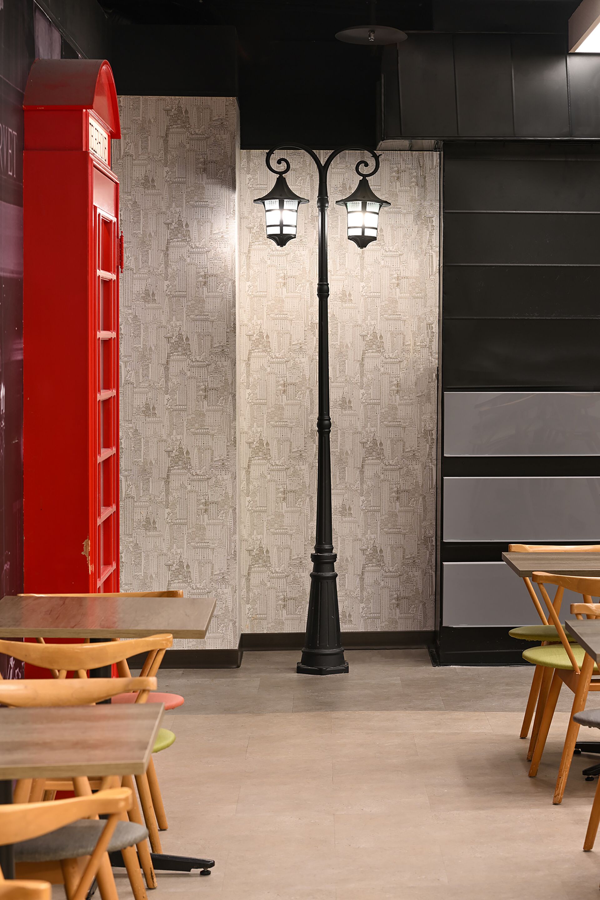 Una habitación con un teléfono rojo, dos lámparas negras fijadas a la pared y mesas y sillas de madera.