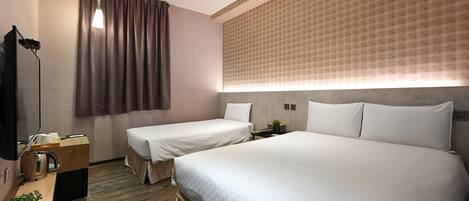 A hotel room with two beds, a desk with a kettle, a small plant, and a wall-mounted TV.