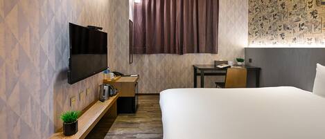 A hotel room with a bed, a desk, a TV, a small table, and a plant.