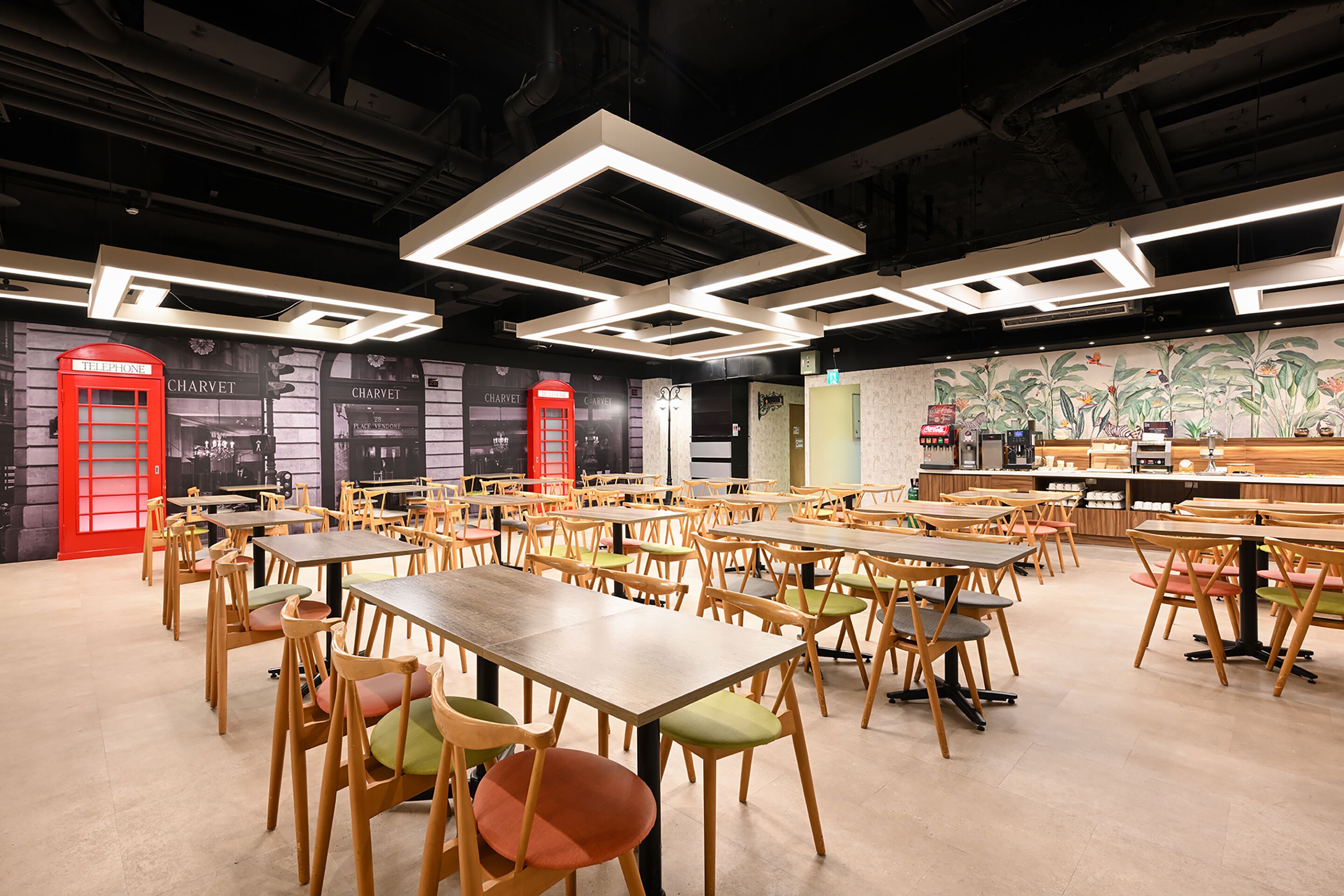 A spacious cafe with multiple tables and chairs, a red telephone booth, and a mural on the wall.