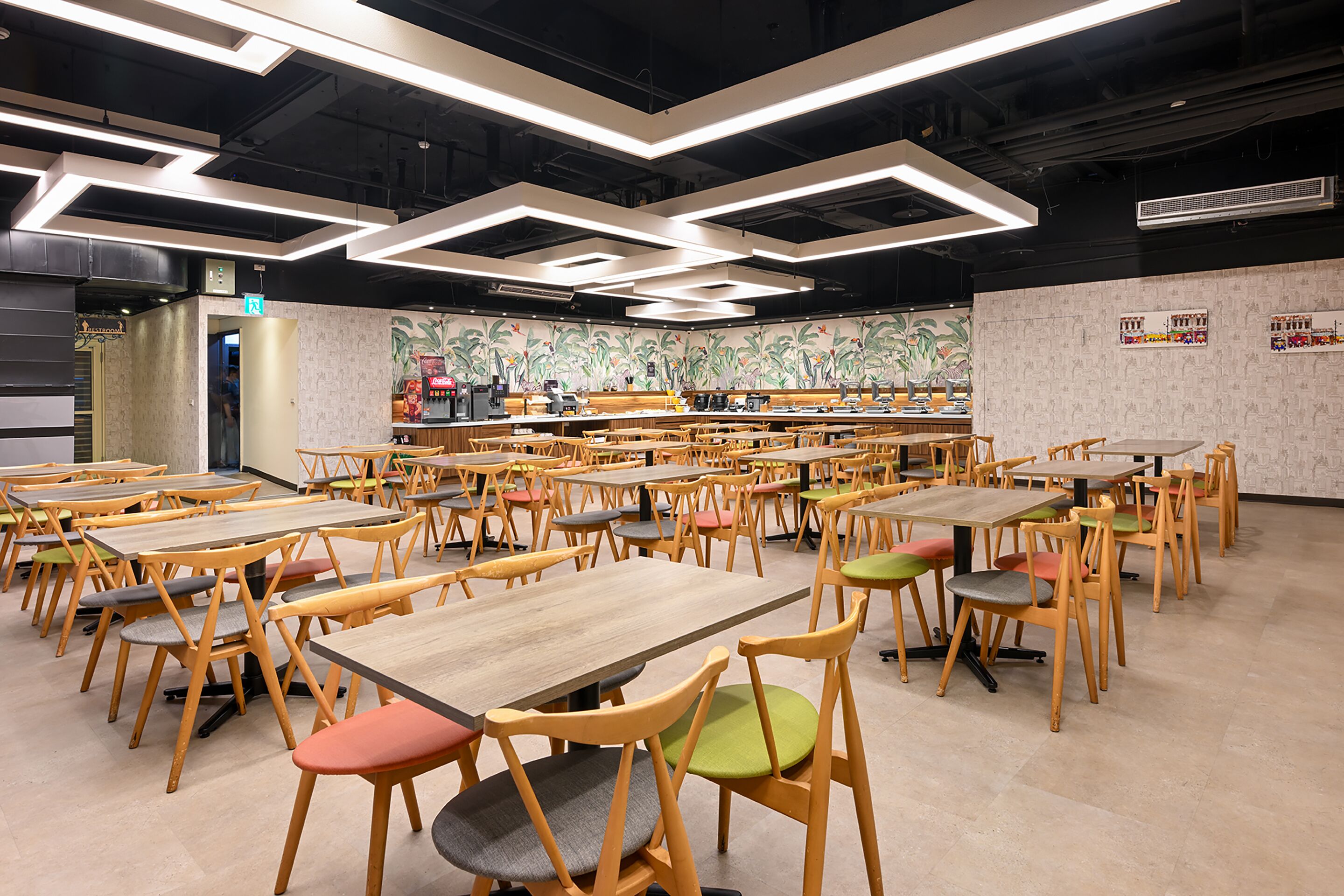 A spacious cafeteria with multiple tables and chairs, a coffee machine, and a mural on the wall.
