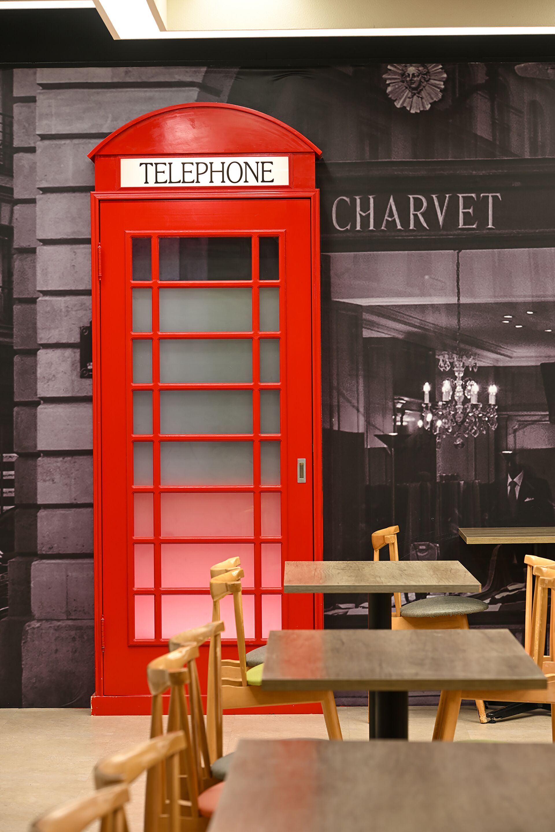 Una cabina telefónica roja con un letrero que dice 'TELEPHONE' junto a un letrero del restaurante Charvet. Hay mesas y sillas de madera en primer plano.