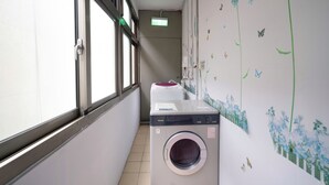A laundry room with a washing machine and dryer, a window, and a wall with a floral mural. - Bon Hotel Taipei (Taipei)
