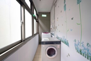 Een wasserette met een wasmachine en droger, een raam, en een muur met een bloemenmuur.